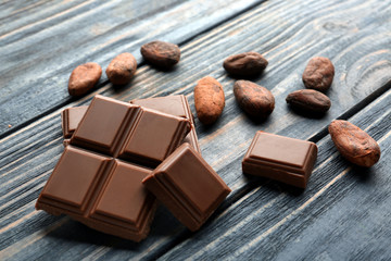 Pieces of tasty milk chocolate and cocoa beans on wooden background