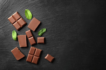 Pieces of tasty milk chocolate and mint leaves on dark background