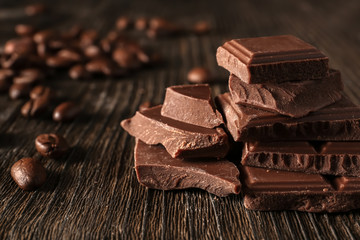Pieces of tasty milk chocolate and coffee beans on wooden background