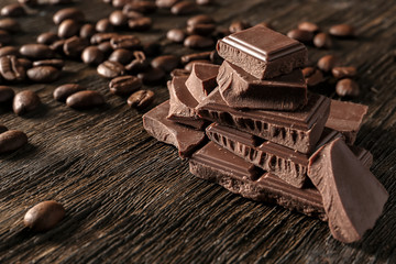 Pieces of tasty milk chocolate and coffee beans on wooden background