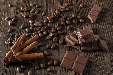 Pieces of tasty milk chocolate and coffee beans on wooden background