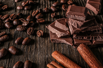 Pieces of tasty milk chocolate, cinnamon sticks and coffee beans on wooden background