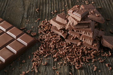 Tasty milk chocolate bar with pieces and shavings on wooden background