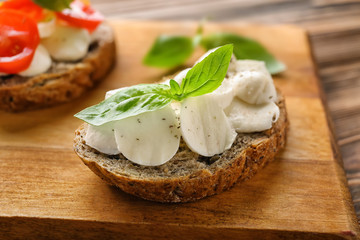 Tasty sandwich with mozzarella and basil on wooden board