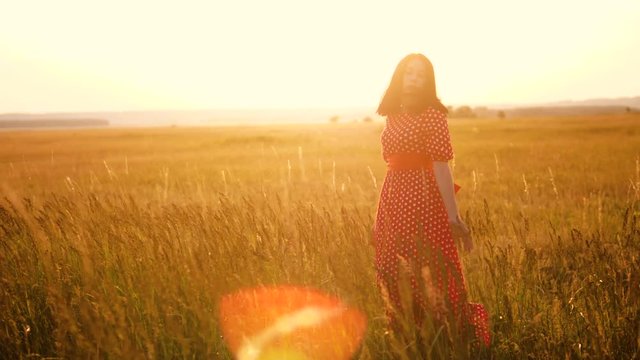 Beautiful young girl walking on field with wildflowers, enjoying nature outdoors Slow motion video. girl in the field at sunset in a red dress lifestyle hand close-up on the grass sunlight silhouette