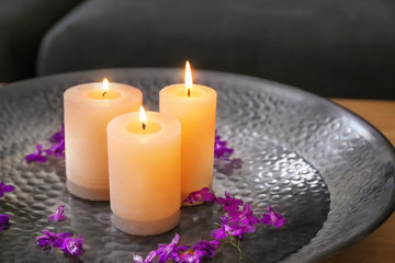 Plate with burning wax candles, water and flower petals on table