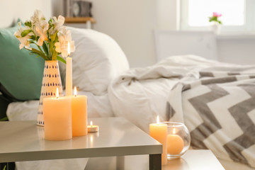 Burning wax candles on table in bedroom
