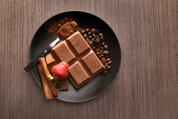 Plate with tasty milk chocolate and strawberry on wooden background