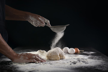 Man sifting flour over dough on black background - Powered by Adobe