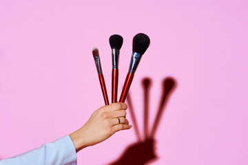 Closeup of female hand holding makeup brushes against purple background. Hard lightining with shade