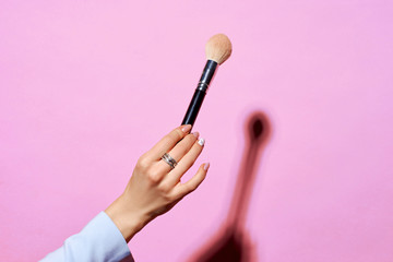 Closeup of female hand holding makeup brushes against purple background. Hard lightining with shade