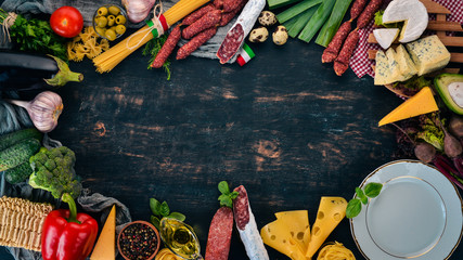 Assortment of sausage, cheese and fresh vegetables. Italian cuisine. On a black wooden background....