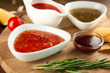 Bowls with different sauces on wooden board, closeup