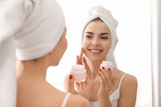 Morning of beautiful young woman applying facial cream in bathroom