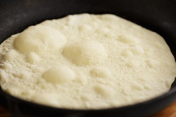 Process of tortilla's cooking on cast iron pan. Bubbles forming on the dough's surface during frying.