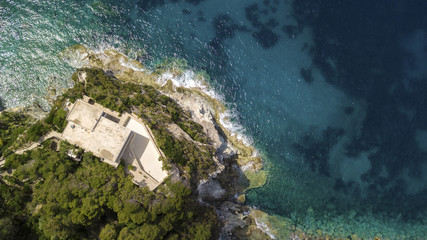 Perpendicular aerial view on a house built near the ocean in California. The waves of the sea collide on the rocky coast on this beautiful summer day.