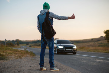 Man with backpack happy hitchhiking on road. Tourist traveler travel auto stop. Adventure, discovery, wanderlust. Hipster hiker show thumbs up hand gesture. Summer vacation concept.