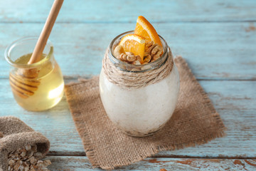 Tasty oatmeal dessert with sliced orange and walnuts in glass jar on wooden background