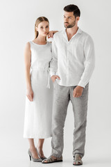 young woman in linen white dress embracing boyfriend with hand in pocket isolated on grey background