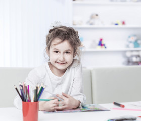 five year old girl draws with crayons sitting at table in the nursery