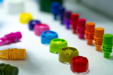 Selective focus on different type of plastic bottle cap of food and drink product. Green, yellow, red, pink, orange, blue, and purple cap closure on white table. Modern design plastic bottle cap.