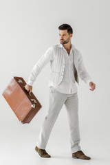 stylish male tourist in linen clothes carrying vintage suitcase isolated on grey background