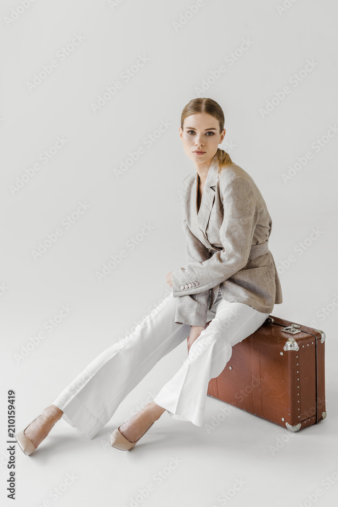 Canvas Prints attractive stylish woman in linen jacket sitting on vintage suitcase isolated on grey background