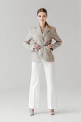 beautiful stylish woman adjusting belt of linen jacket isolated on grey background
