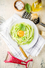 Trendy vegan food recipes, cheese zucchini spaghetti pasta with egg yolk with parmesan, olive oil and basil leaves, light concrete background copy space