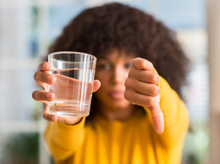African american woman drinking a glass of water at home with angry face, negative sign showing...