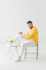 attractive young man in yellow hoodie sitting on chairs on white