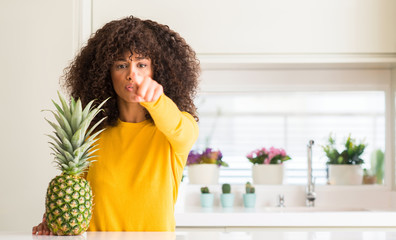 African american woman and pineapple tropical fruit pointing with finger to the camera and to you,...
