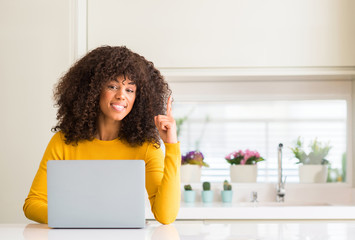 African american woman using computer laptop at kitchen surprised with an idea or question pointing...