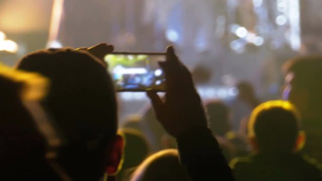 People at Music Rock Concert Taking Photos or Recording Video with Smartphones. Fan person filming on mobile smart phone at concert party crowd cheering at rock music event with flashing light show