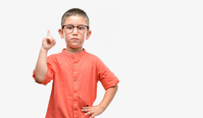 Dark haired little child wearing glasses surprised with an idea or question pointing finger with...