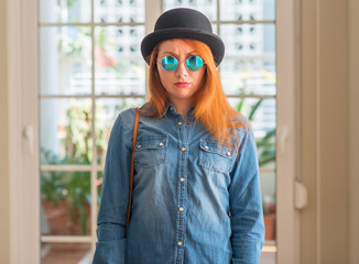 Stylish redhead woman wearing bowler hat and sunglasses skeptic and nervous, frowning upset because...