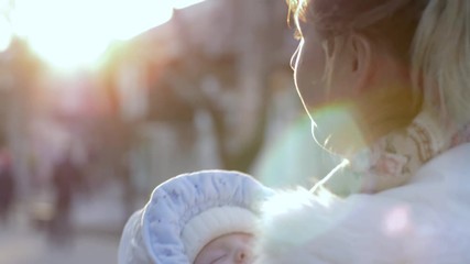 young woman with sleeping infant in hands sings on open air in sun rays close-up
