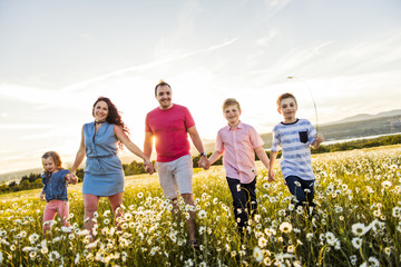 Happy family having fun on daisy field at sunset