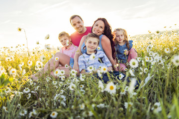 Happy family having fun on daisy field at sunset