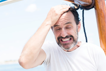 Handsome senior man traveling on sailboat stressed with hand on head, shocked with shame and...
