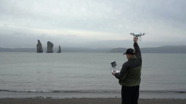 Man catches quadcopter with attached 360-degree camera in beach of Pacific Coast after flying and shooting islands in sea on cloudy weather. Eurasia, Russian Far East, Kamchatka Peninsula, Avacha Bay.