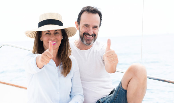 Middle age couple traveling on sailboat happy with big smile doing ok sign, thumb up with fingers, excellent sign