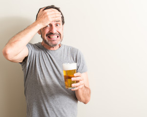 Fototapeta premium Senior man drinking beer stressed with hand on head, shocked with shame and surprise face, angry and frustrated. Fear and upset for mistake.