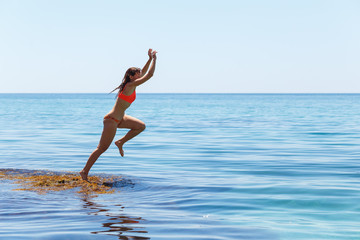 Fototapeta na wymiar A girl is jumping into the sea water. Summer mood. Vacation at sea. Beautiful jump of a young woman in a swimsuit. Fuss and fun.
