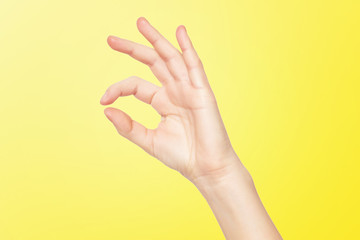 Closeup female hand making OK gesture isolated at yellow background.