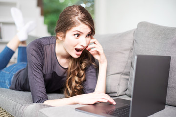 Junge Frau sympathisch lachend mit Laptop auf der Couch