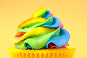 Cupcake with rainbow colorful cream on yellow background. Close up.