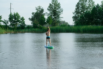 Fototapeta na wymiar A man stands on a SAP Board with an oar and swims through a forest lake,