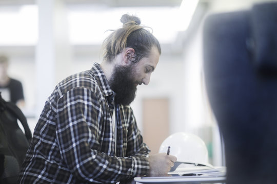 Man sitting at a table writing with safety helmet next to him