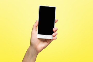 Mockup of female hand holding frameless cell phone with black screen isolated at yellow background.